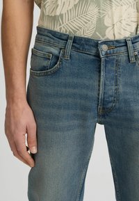 Jeans de mezclilla azul claro con un corte ajustado, que cuentan con un diseño clásico de cinco bolsillos y un ligero desgastado. La cinturilla tiene un cierre de botón metálico.