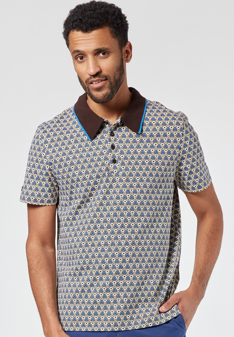 Lyhythihainen polo-paita, jossa on sinivalkoinen kuvioitu kangas, ruskeat kaulukset sinisillä yksityiskohdilla ja nappikiinnitys edessä.