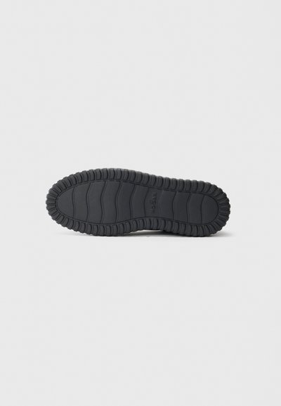 Black rubber shoe sole with deep tread patterns and brand name embossed in the center, displayed on a white background.