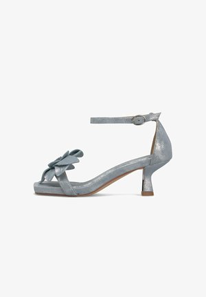 Sandale argentée à bout ouvert avec talon bloc bas, bride à la cheville avec boucle, et nœud décoratif orné de petites pierres précieuses sur la bride avant.