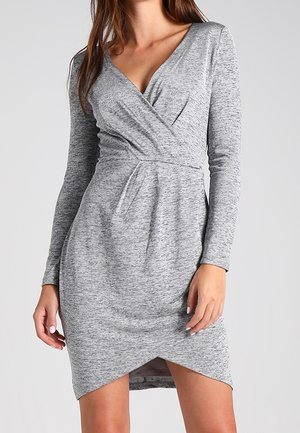 Woman wearing a fitted, long-sleeve, gray knit dress with a V-neck wrap front and asymmetrical hem.