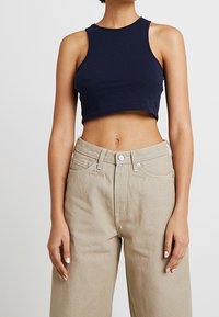 Námořnický zkrácený tílko vyrobené z jemné bavlny, spárované s béžovými širokými kalhotami s vysokým pasem, které mají zapínání na knoflík a kapsy.