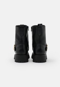 Ein Paar schwarze Lederstiefeletten mit dicken Sohlen, Rückreißverschlüssen und dekorativen seitlichen Schnallen auf einem schlichten, hellen Hintergrund.