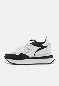 Baskets à plateforme blanches et noires avec lacets à l'avant et détails en clous dorés formant un motif circulaire sur le côté.