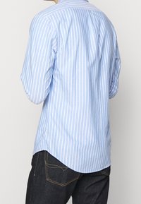 Niebieska i biała w paski koszula z długim rękawem z tylnym yoke, zaokrąglonym dołem i nieco luźnym krojem, wykonana z lekkiego materiału.