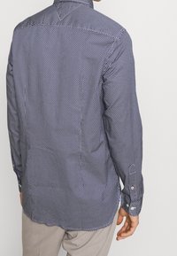 Camicia a maniche lunghe di colore blu navy con un piccolo motivo a pois bianchi. Presenta un colletto e polsini con bottoni, realizzata in tessuto liscio.