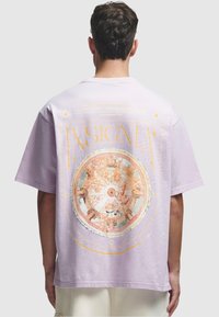 Lys lilla oversized t-skjorte med et sirkulært, flerfarget grafikk på baksiden med intrikate design og gullakenter.
