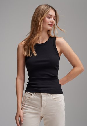 Top a maniche corte nero a coste senza maniche con scollatura rotonda, abbinato a jeans beige chiaro aderenti, che mettono in risalto una consistenza liscia e una vestibilità slim.