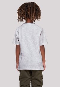 Camiseta gris de manga corta vista desde la espalda, con un escote redondeado y una textura lisa y jaspeada. Llevada con pantalones cargo color oliva.