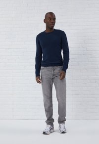 Marineblauwe gebreide trui met lange mouwen, gecombineerd met lichtgrijze jeans en zilveren sportschoenen. Eenvoudig, aansluitend design met geribbelde manchetten.