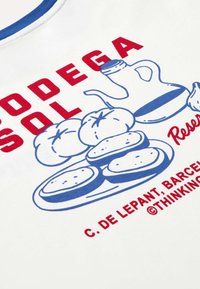 Graphique bleu et rouge sur tissu blanc montrant des tomates, trois tranches de pain sur une assiette, et une carafe avec un texte rouge indiquant "Bodega Sol."