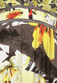 Tkanina z warstwowymi falbanami przedstawiająca tropikalny wzór kwiatowy w żółtych, pomarańczowych, brązowych i białych odcieniach z widocznymi szwami.