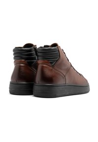 Brązowe skórzane bardzo wysokie buty z eleganckim wzornictwem, z czarną wyściółką u góry, sznurowanym przodem i teksturowaną gumową podeszwą.