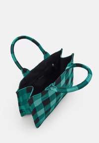 Sac fourre-tout à carreaux verts et noirs avec deux poignées. L'intérieur présente une doublure noire et une poche zippée. La texture du tissu est tissée.