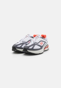 Une paire de chaussures de sport blanches et grises avec des accents orange et des semelles texturées sur un fond clair.
