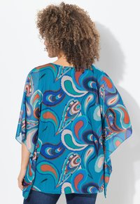 Gennemsigtig turkis kimono med et paisley-mønster i rød, blå og hvid. Løs pasform med brede ærmer og en buet kant.