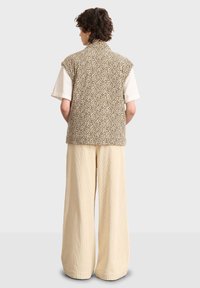 Tunn ärmlös väst med en fläckig leopardprick, i kombination med en vit T-shirt och vida beige kordbyxor. Strukturerad tygkvalitet och avslappnad passform.