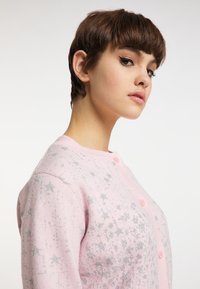 Cardigan roz cu model de stele argintii, cu nasturi în față, guler ribonat și o textură moale. Design cu mâneci scurte, stil fitted.