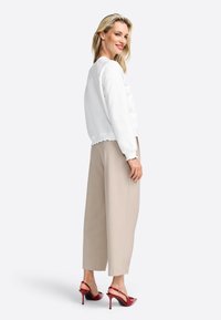Felpa bianca a taglio corto con orlo a scallop, abbinata a pantaloni beige a gamba larga e décolleté slingback in pelle rossa lucida. Sfondo semplice.