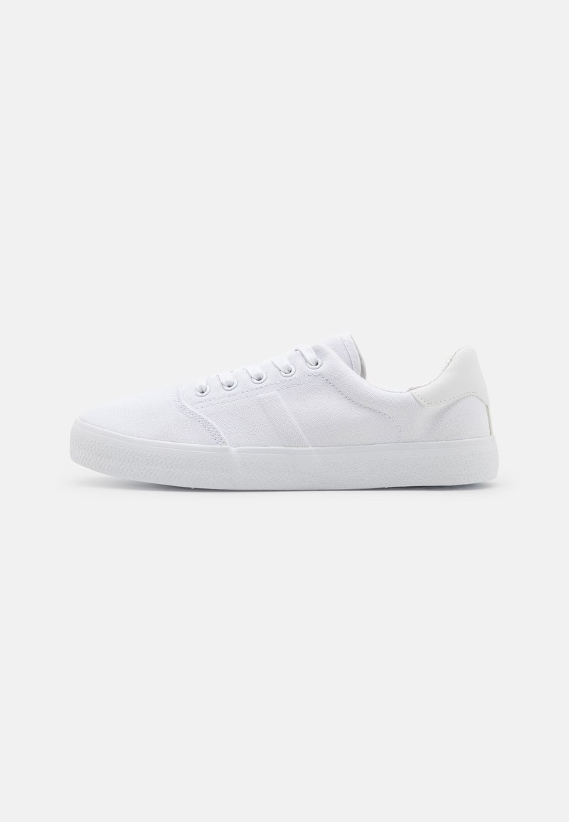 Sneakers bianchi in tela con suola in gomma, caratterizzati da sei fori per i lacci, una punta testurizzata e un design minimalista.