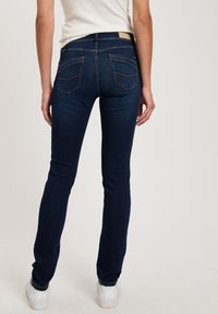 Dark blue skinny jeans made of denim, with a smooth texture, slightly faded at the thighs, featuring two back pockets and a waistband tag.