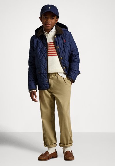 Temno modra prešita jakna z rjavim ovratnikom, rdeče-belo črtast pulover, kaki hlače in rjavi loaferji. Obleko dopolnjuje modra kapa.