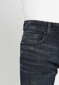 Mörkblå denimjeans med slim fit, med lätt blekning och slitna detaljer. Inkluderar fem fickor och orangea sömnadsdetaljer.