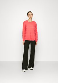 Haut à manches longues rose avec des rayures texturées, associé à un pantalon large noir. Le mannequin porte des baskets blanches et noires. Design simple et moderne.