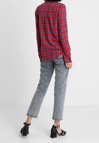 Röd och blå rutiga skjorta med knäppning, kombinerad med ljusgrå, texturerade raka jeans och svarta högklackade sandaler.