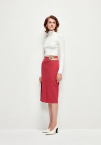 Pull en maille côtelée blanche à col roulé ajusté, jupe crayon rouge mi-longue avec une fente sur le côté, et escarpins blancs avec des accents de talons noirs.