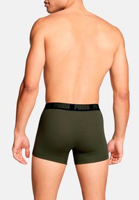 Grüne Boxershorts mit einem schwarzen Bündchen, das das "PUMA"-Logo trägt. Der Stoff wirkt glatt und eng anliegend, mit einem schlichten Design.