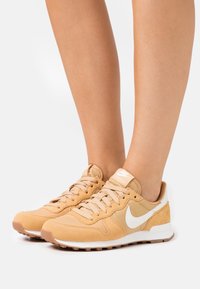 Beige mockasins och nät sneakers med en vit swoosh, texturerade detaljer och beige snören. Gummisula med greppmönster.