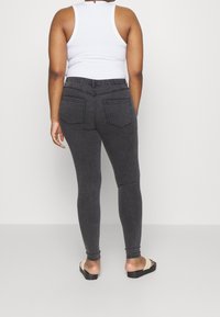 Vaqueros elásticos de color gris oscuro con un diseño ajustado, bolsillos traseros y una textura suave, combinados con una camiseta sin mangas blanca y sandalias.