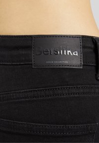 Mustat farkut sisältävät nahkaleiman, johon on painettu "Bershka" ja "DENIM COLLECTION" -teksti, mikä korostaa tyylikästä ja modernia muotoilua.