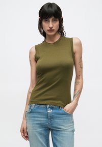 Top sin mangas color verde oliva con textura acanalada y escote redondo, combinado con vaqueros de mezclilla azul claro. Diseño ajustado.