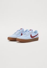 Lyseblå sneakers fremstillet af stof og gummi, med en rød Nike swoosh, flade snørebånd og en brun gummisål.