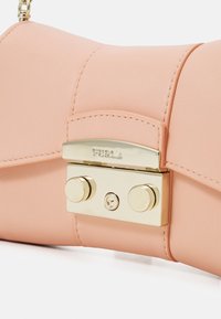 Růžová kožená kabelka se zlatým sponou ve tvaru klipsu s dvěma kulatými knoflíky a s embosovaným logem na přední straně. Hladký povrch.