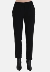 Zwarte tappered broek met een elastische tailleband, zijzakken en opgerolde boorden, gecombineerd met puntige zwarte enkellaarsjes.