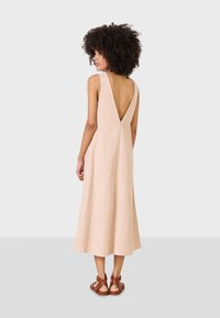Vestido midi de lino beige con escote en V profundo, diseño sin mangas y silueta fluida. Combinado con sandalias marrones de tiras.