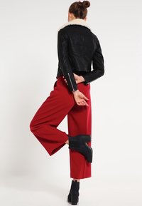 Chaqueta de cuero negra con cuello de piel blanca, pantalones rojos de pierna ancha y botines negros. Enfócate en la textura y los colores contrastantes.