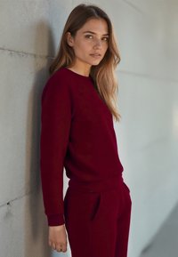 Bordeaux sweatshirt en bijpassende joggers van een gladde stof. De sweatshirt heeft een ronde halslijn en ribgebreide boorden, met zijzakken op de joggers.