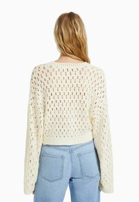 Krämfärgad stickad kort tröja med öppen gallerdesign, ribbade ärmslut och nederkant. Matchad med ljusblå denimjeans.