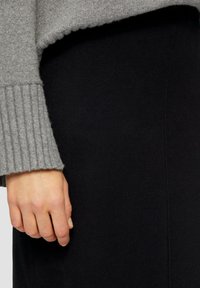 Grijze gebreide trui met geribde cuffs, gecombineerd met een aansluitende zwarte rok. Focus op de textuur van het materiaal en het kleurcontrast.
