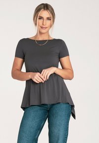 Szary top z krótkim rękawem i rozkloszowanym dołem, wykonany z miękkiego, elastycznego materiału. Połączony ze średnio niebieskimi dżinsami. Prosty, okrągły dekolt.