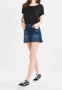 Un haut noir à manches courtes associé à une mini-jupe en denim bleu. L'ensemble est complété par des baskets noires avec des accents blancs.