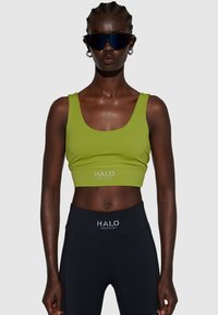Grøn, cropped tanktop med rund udskæring, parret med højtaljede sorte leggings, som har et hvidt logo ved taljen. Glat tekstur.