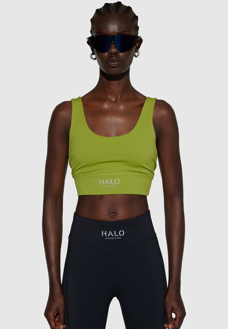 Grøn, cropped tanktop med rund udskæring, parret med højtaljede sorte leggings, som har et hvidt logo ved taljen. Glat tekstur.
