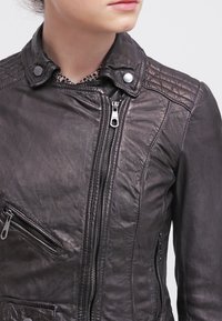 Sort lædermotorcykeljakke med quiltet skulderdesign, lynlåslukning foran og to lynlåslommer. Glat tekstur og tætsiddende form.