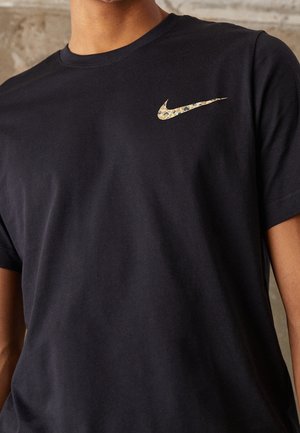 T-shirt en coton noir avec un logo Nike swoosh doré et à motif sur la poitrine gauche. Col rond avec manches courtes.