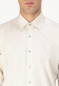 Lys beige skjorte med knappelukking som har et teksturert mønster, en klassisk krage og sølvknapper foran.